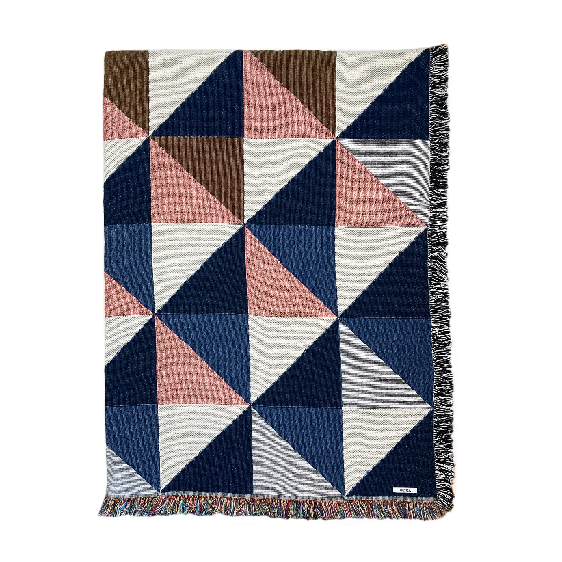A woven cotton throw blanket with a geometric pattern in navy, pink, ochre, and gray, featuring a fringe edge.