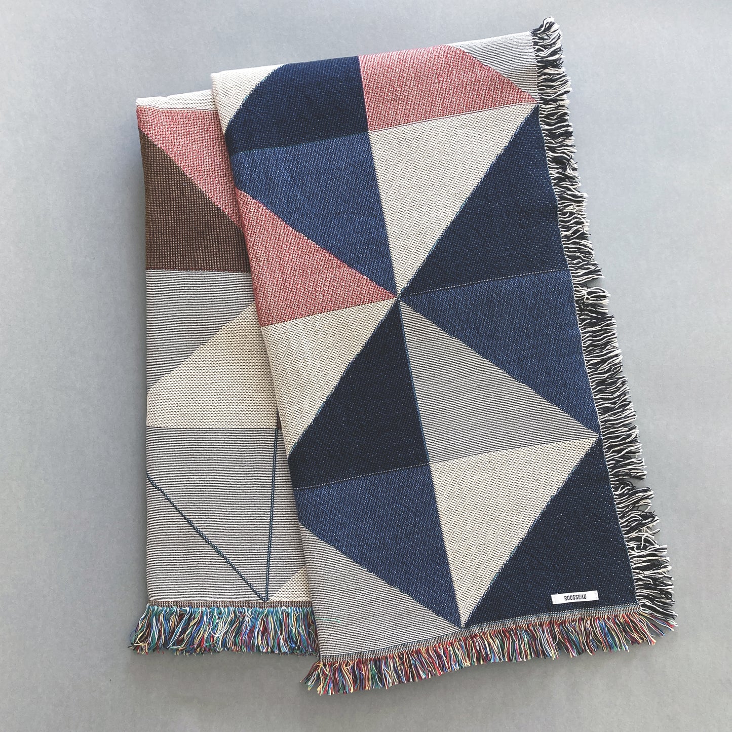 The Sixteen throw in navy, pink, ochre and gray geometric print woven throw with fringe edge. Woven with recycled cotton on a jacquard loom, made in the US. Each throw measures 54 x 72 inches.

This geometric patterned throw is inspired by a painting we created for our New York City studio.
