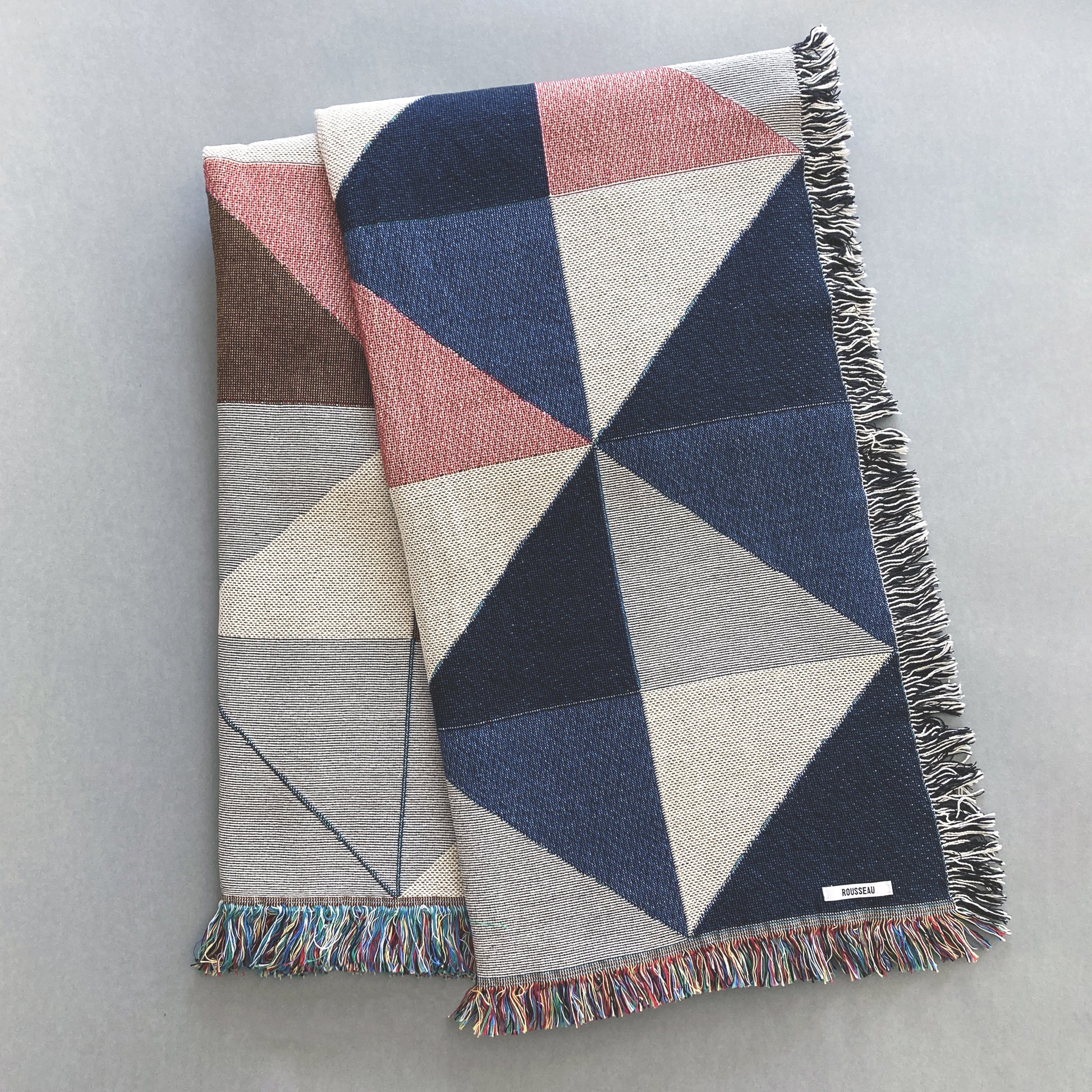 The Sixteen throw in navy, pink, ochre and gray geometric print woven throw with fringe edge. Woven with recycled cotton on a jacquard loom, made in the US. Each throw measures 54 x 72 inches.

This geometric patterned throw is inspired by a painting we created for our New York City studio.