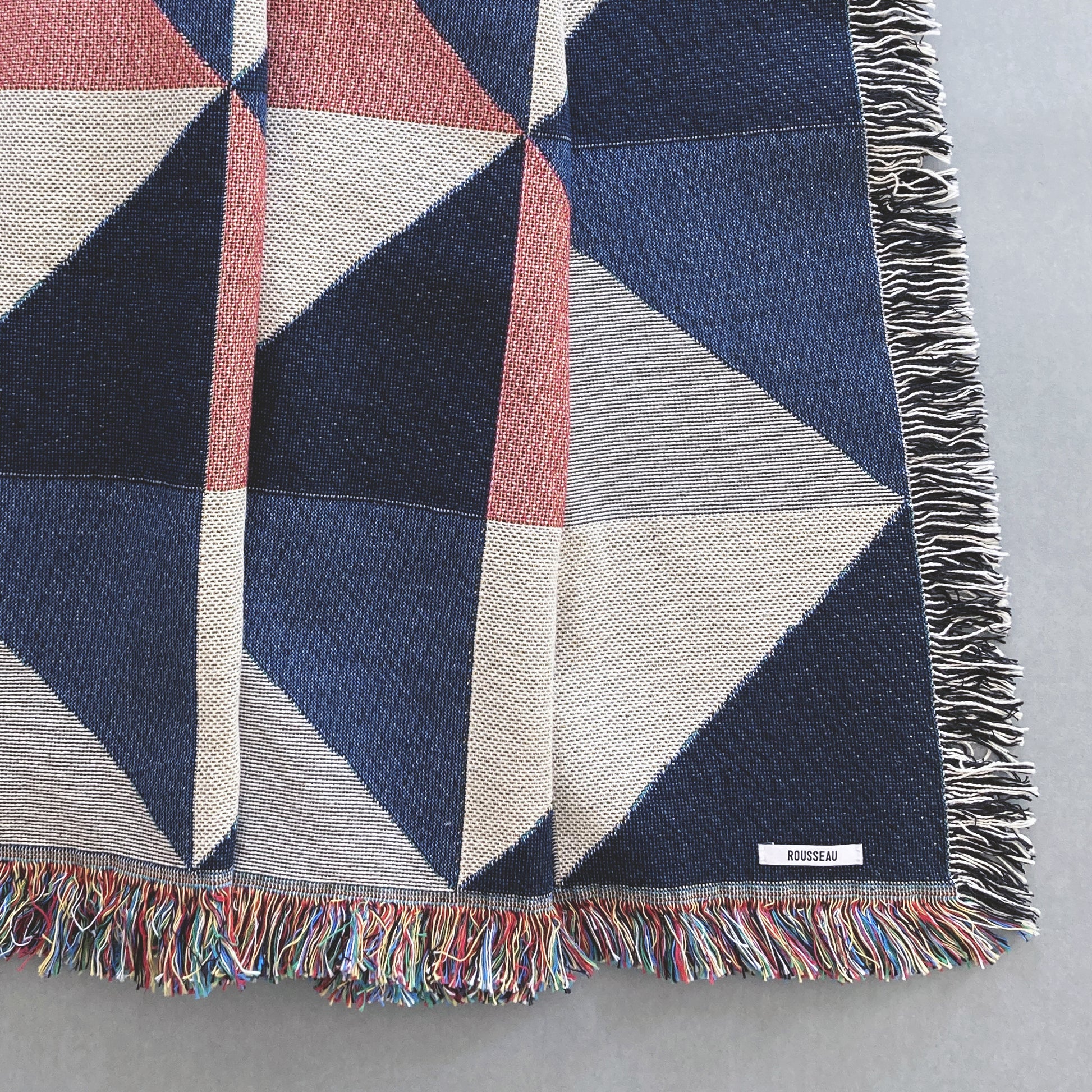 The Sixteen throw in navy, pink, ochre and gray geometric print woven throw with fringe edge. Woven with recycled cotton on a jacquard loom, made in the US. Each throw measures 54 x 72 inches.

This geometric patterned throw is inspired by a painting we created for our New York City studio.