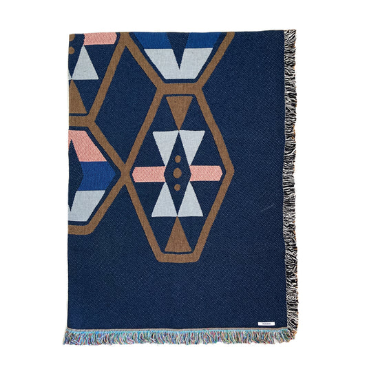 A woven cotton throw blanket with a geometric pattern in navy and contrasting colors, featuring a fringe edge.