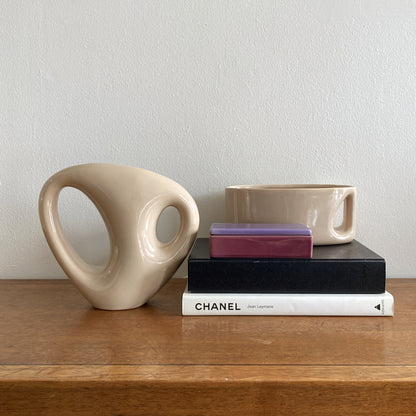 An oblong beige/ecru ceramic vase with a postmodern design, featuring a cut-out on the side.