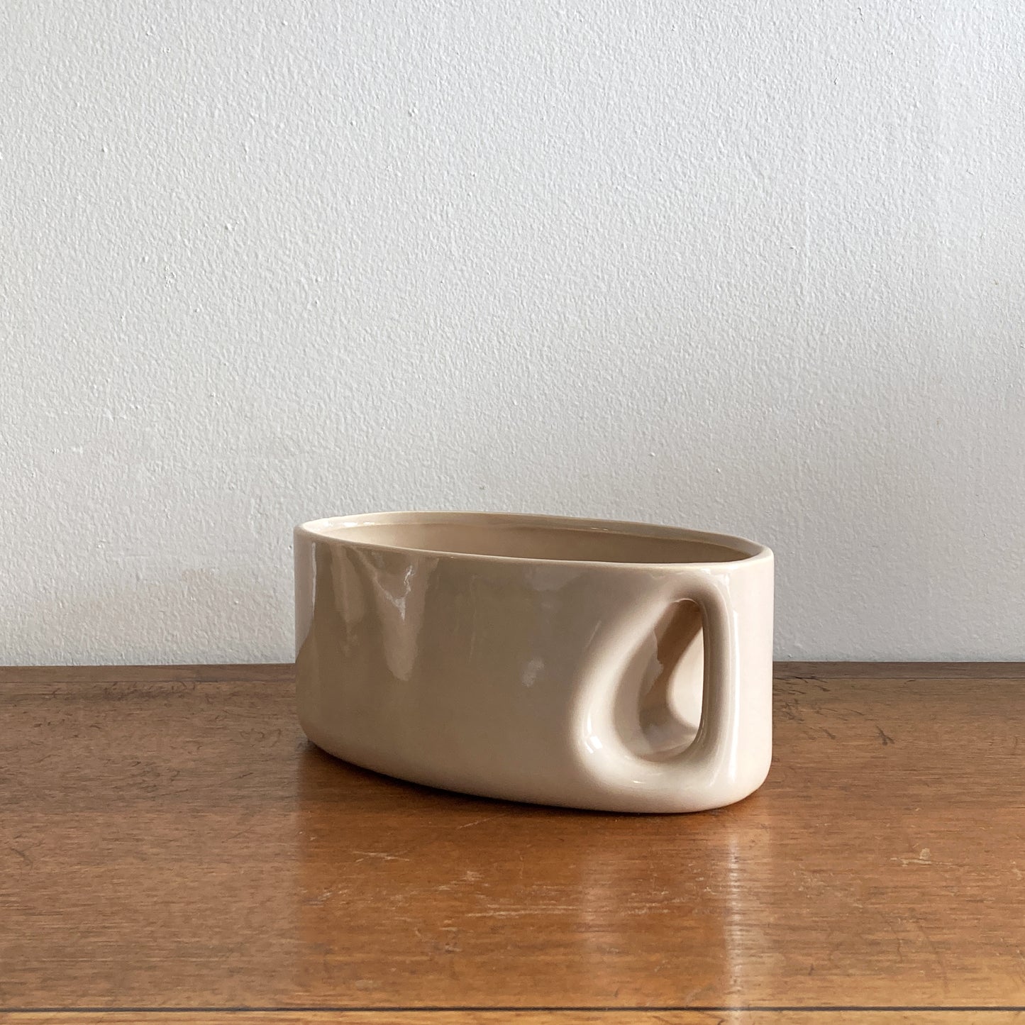An oblong beige/ecru ceramic vase with a postmodern design, featuring a cut-out on the side.