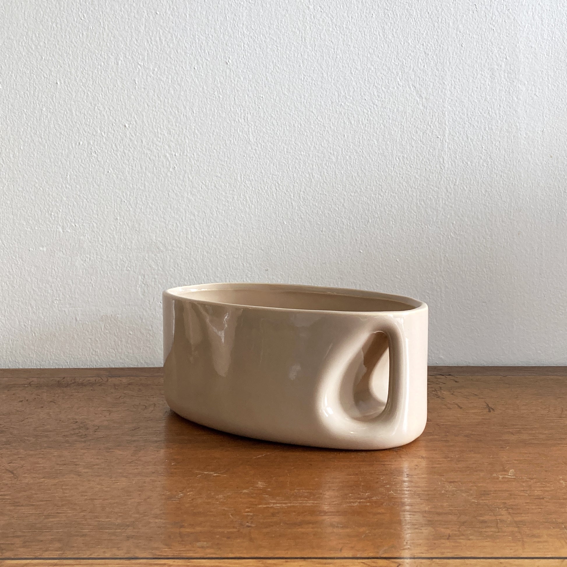 An oblong beige/ecru ceramic vase with a postmodern design, featuring a cut-out on the side.