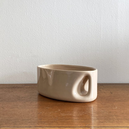 An oblong beige/ecru ceramic vase with a postmodern design, featuring a cut-out on the side.
