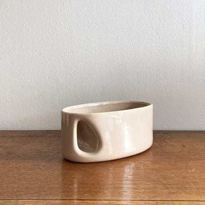 An oblong beige/ecru ceramic vase with a postmodern design, featuring a cut-out on the side.