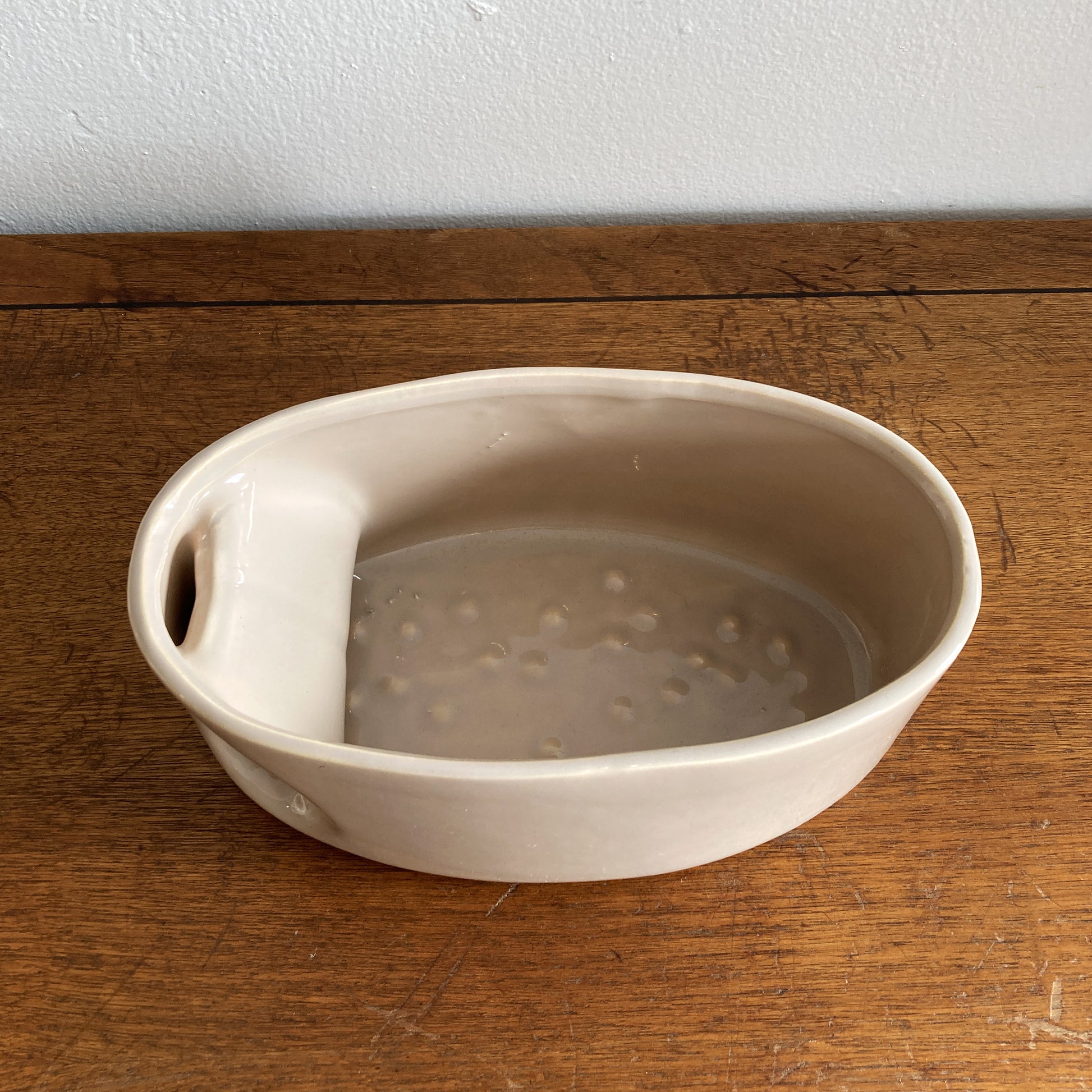 An oblong beige/ecru ceramic vase with a postmodern design, featuring a cut-out on the side.